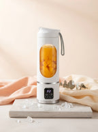 A sleek portable digital blender with a fruit smoothie and crushed ice, set on a stone surface with soft cream and peach deco